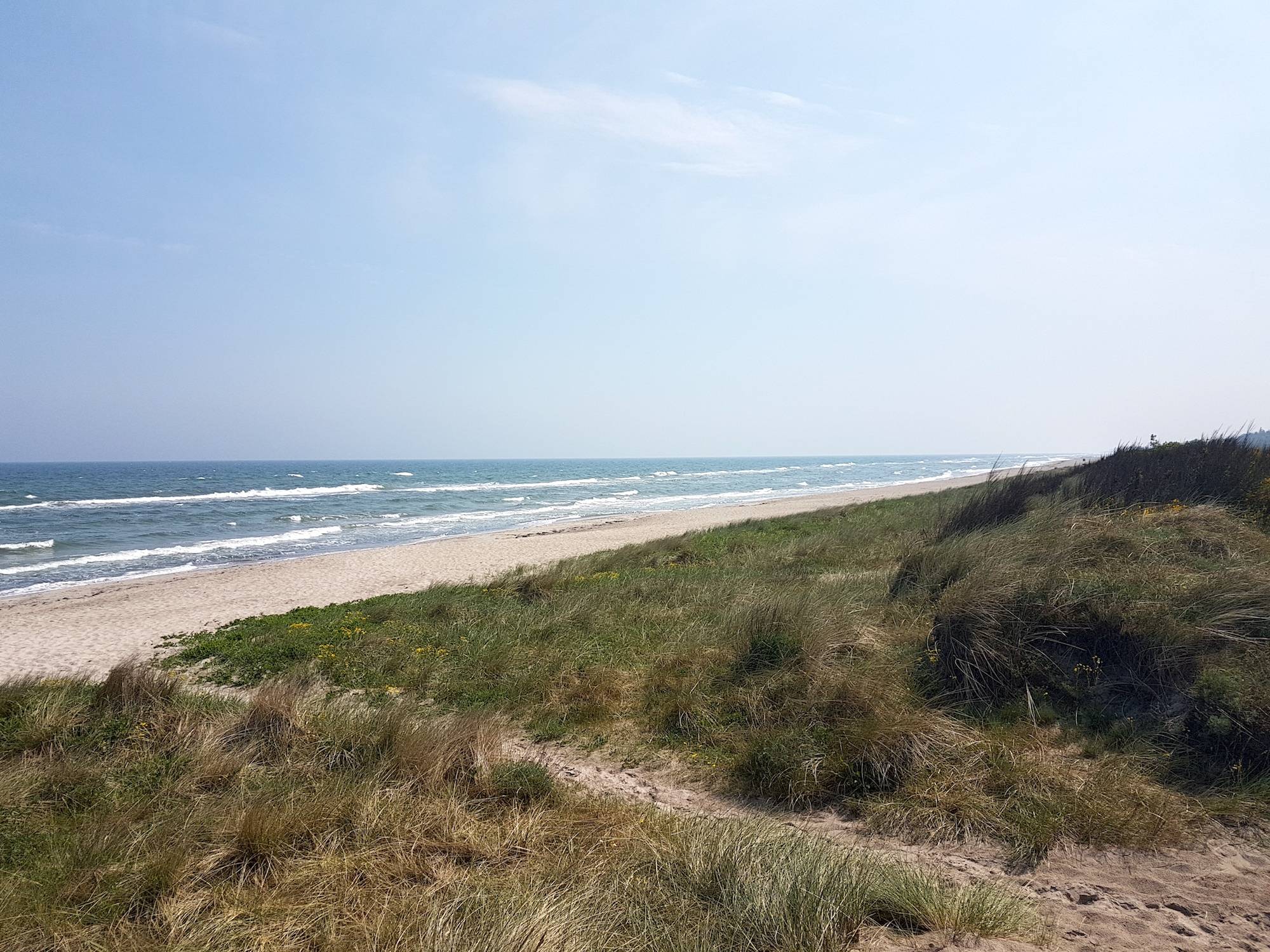Sandstrand mit flachen Dünen und blauer Himmel