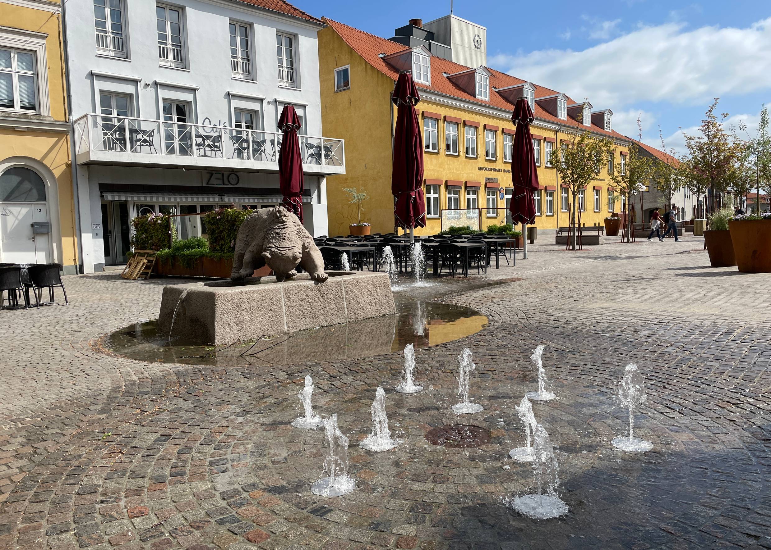 Fußgängerzone mit kleinen älteren Häusern, in der Mitte kleine Wasserfontänen