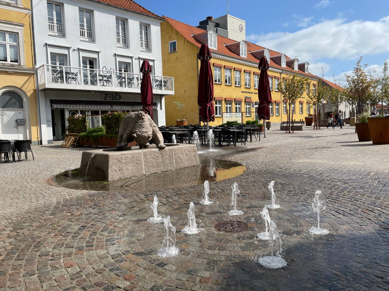 Fußgängerzone mit kleinen älteren Häusern, in der Mitte kleine Wasserfontänen