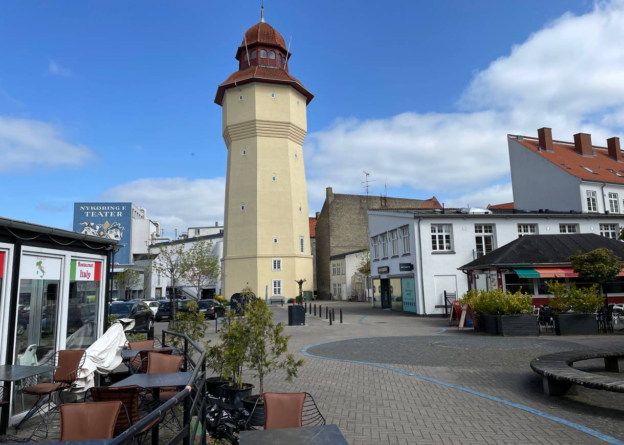 Alter, gelber Wasserturm an einem Platz mit Gastronomie und Bänken