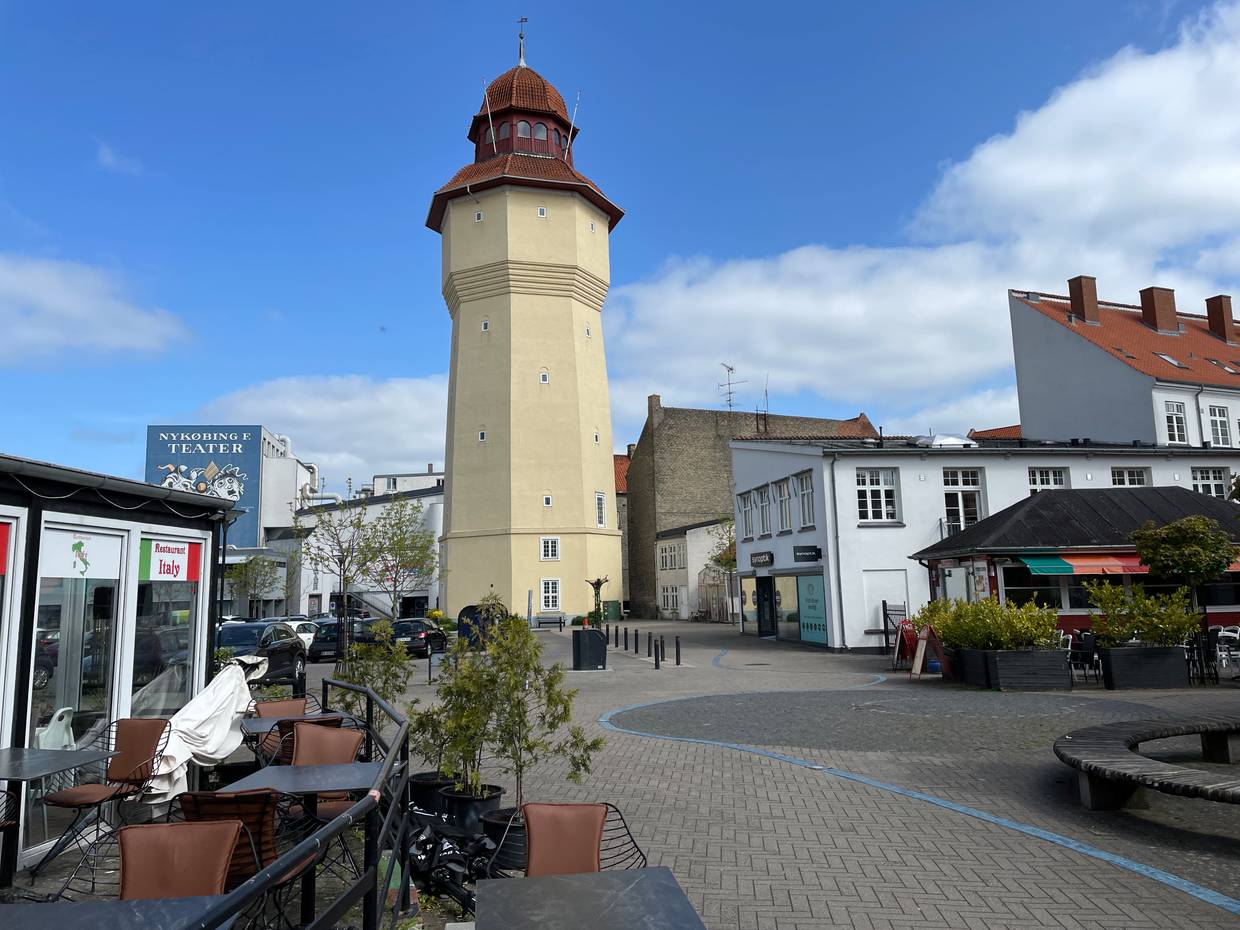 Alter, gelber Wasserturm an einem Platz mit Gastronomie und Bänken