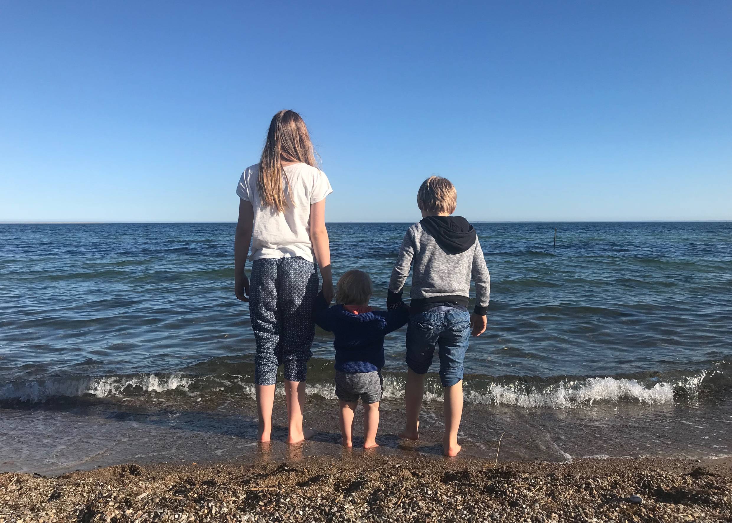 Drei Kinder Hand in Hand mit den Füßen im Wasser