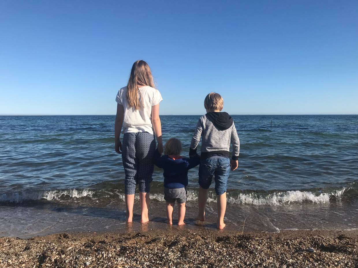 Drei Kinder Hand in Hand mit den Füßen im Wasser