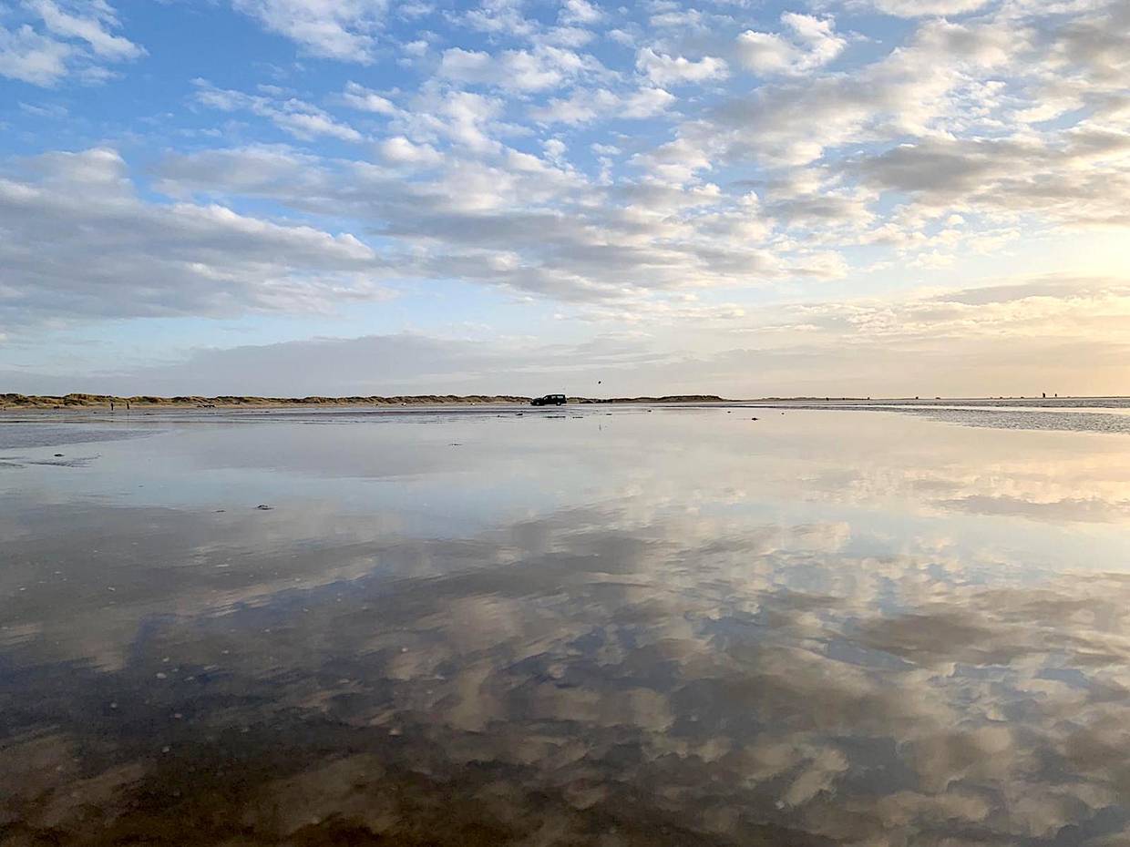 Spiegelnde Wasserfläche auf dem Strand, dahinter ein Auto