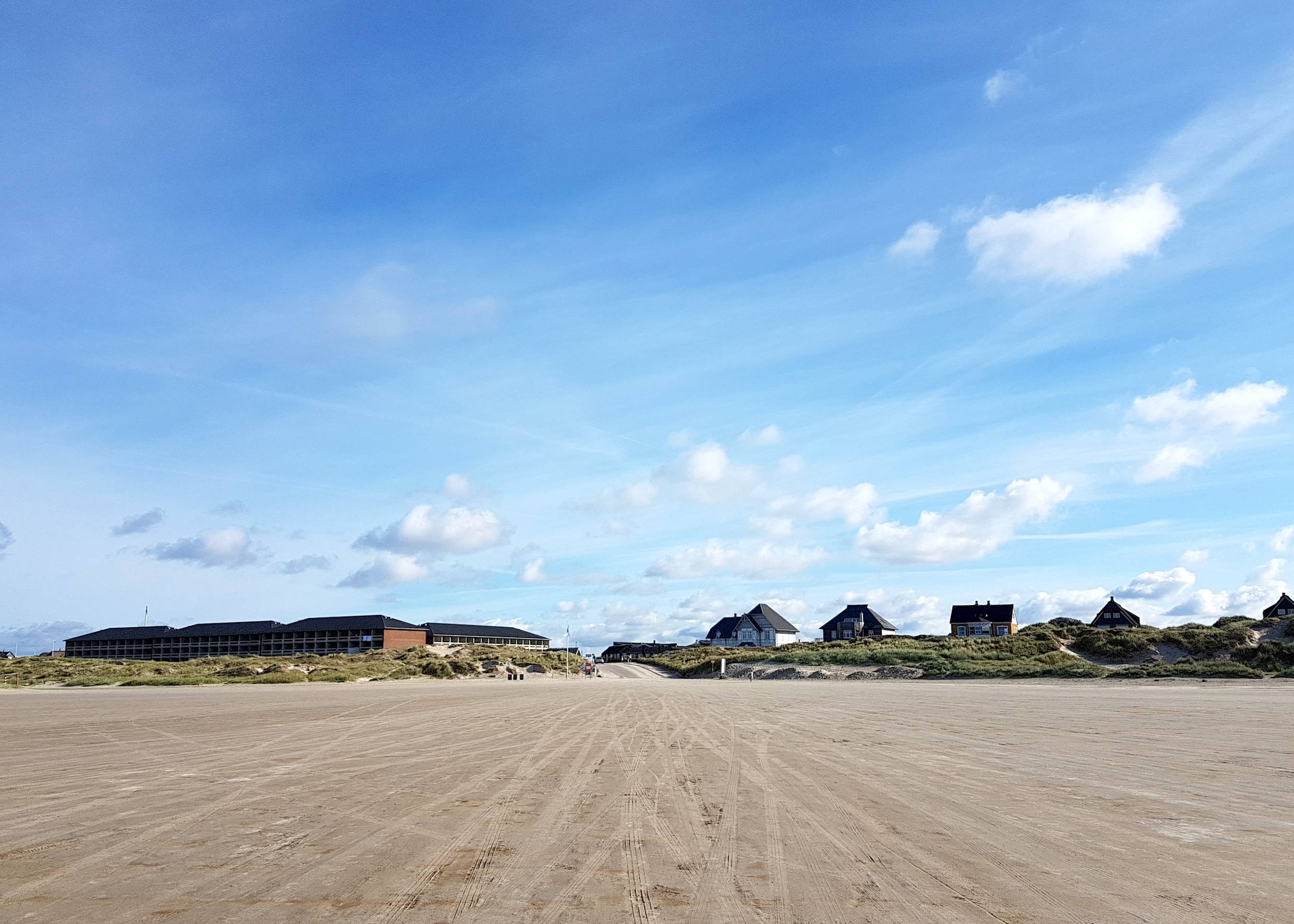 Blick von Strand auf eine Zufahrt zwischen ferienhäusern und Dünen