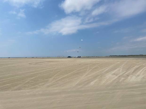 Sehr breiter Sandstrand mit einigen Autos und Drachen am Himmel