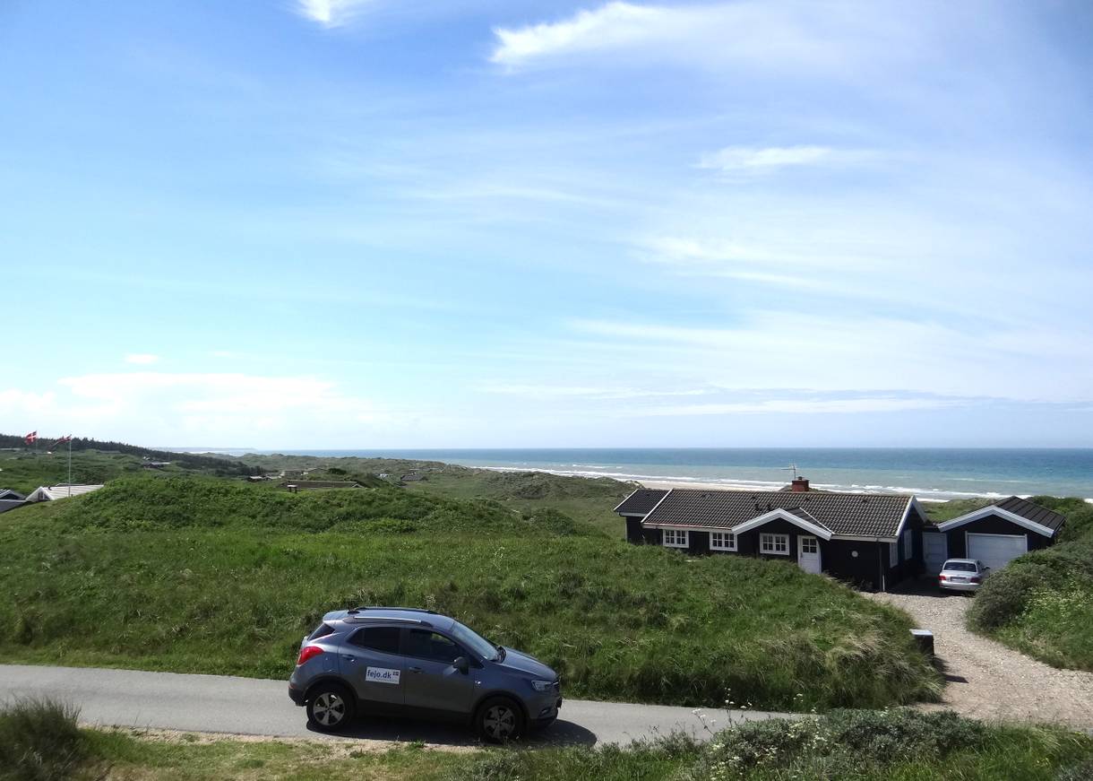 Auto mit fejo-Ausflekber vor einem Ferienhaus, Meer im Hintergrund