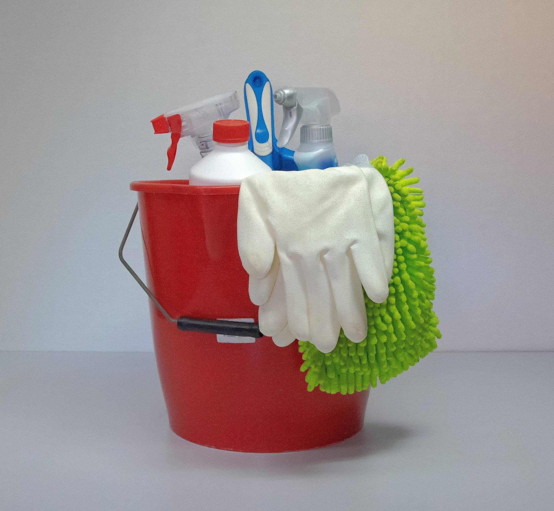 Roter Eimer mit Outzhandschuhen und Sprühflaschen mit Reinigungsmitteln