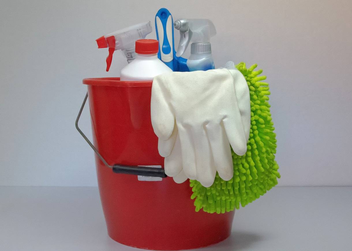 Roter Eimer mit Outzhandschuhen und Sprühflaschen mit Reinigungsmitteln