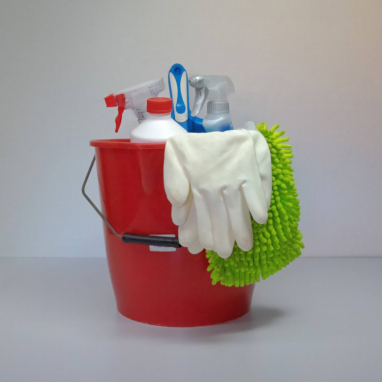 Roter Eimer mit Outzhandschuhen und Sprühflaschen mit Reinigungsmitteln