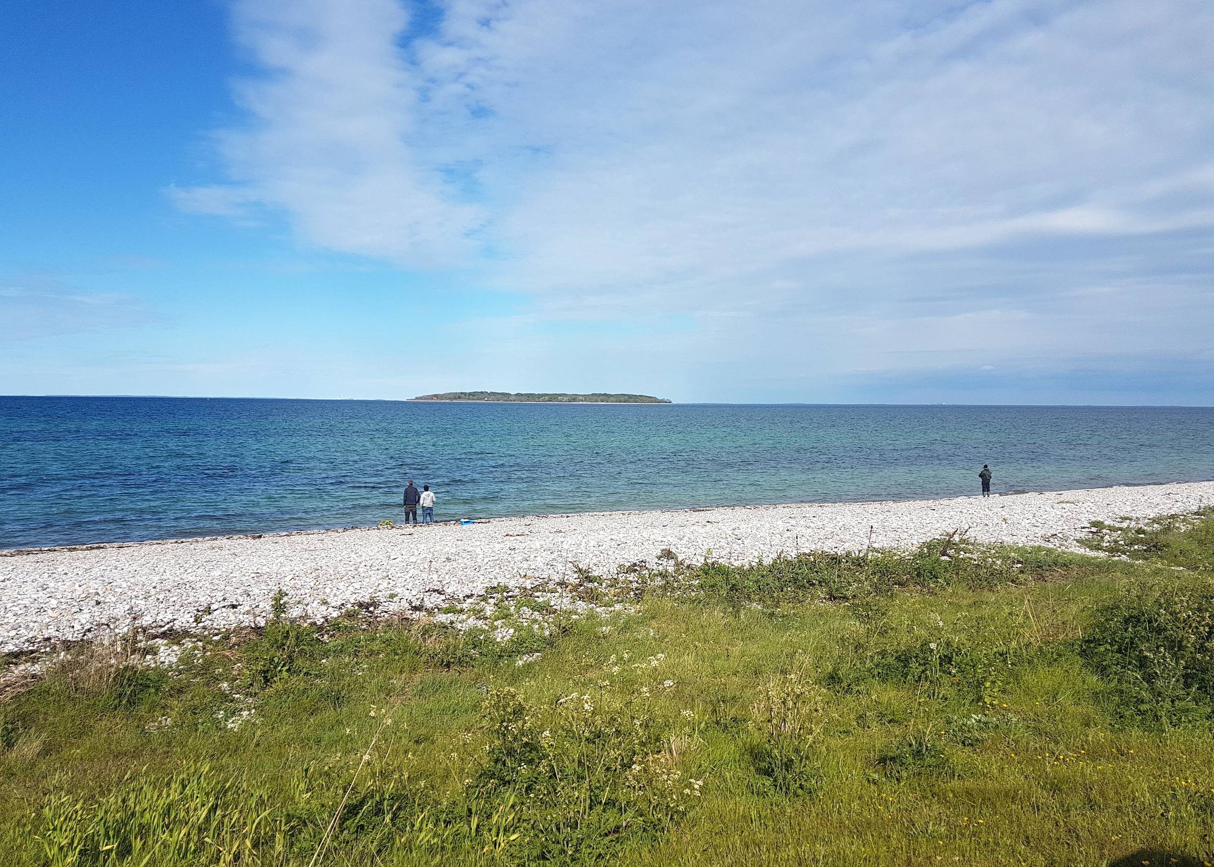 Angler am Steinstrand, im Meer eine kleine Insel
