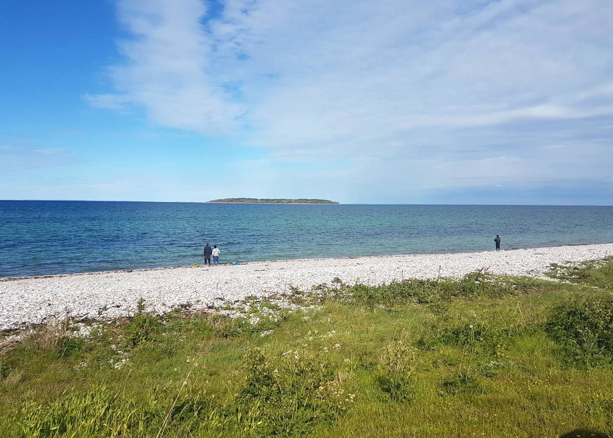 Angler am Steinstrand, im Meer eine kleine Insel