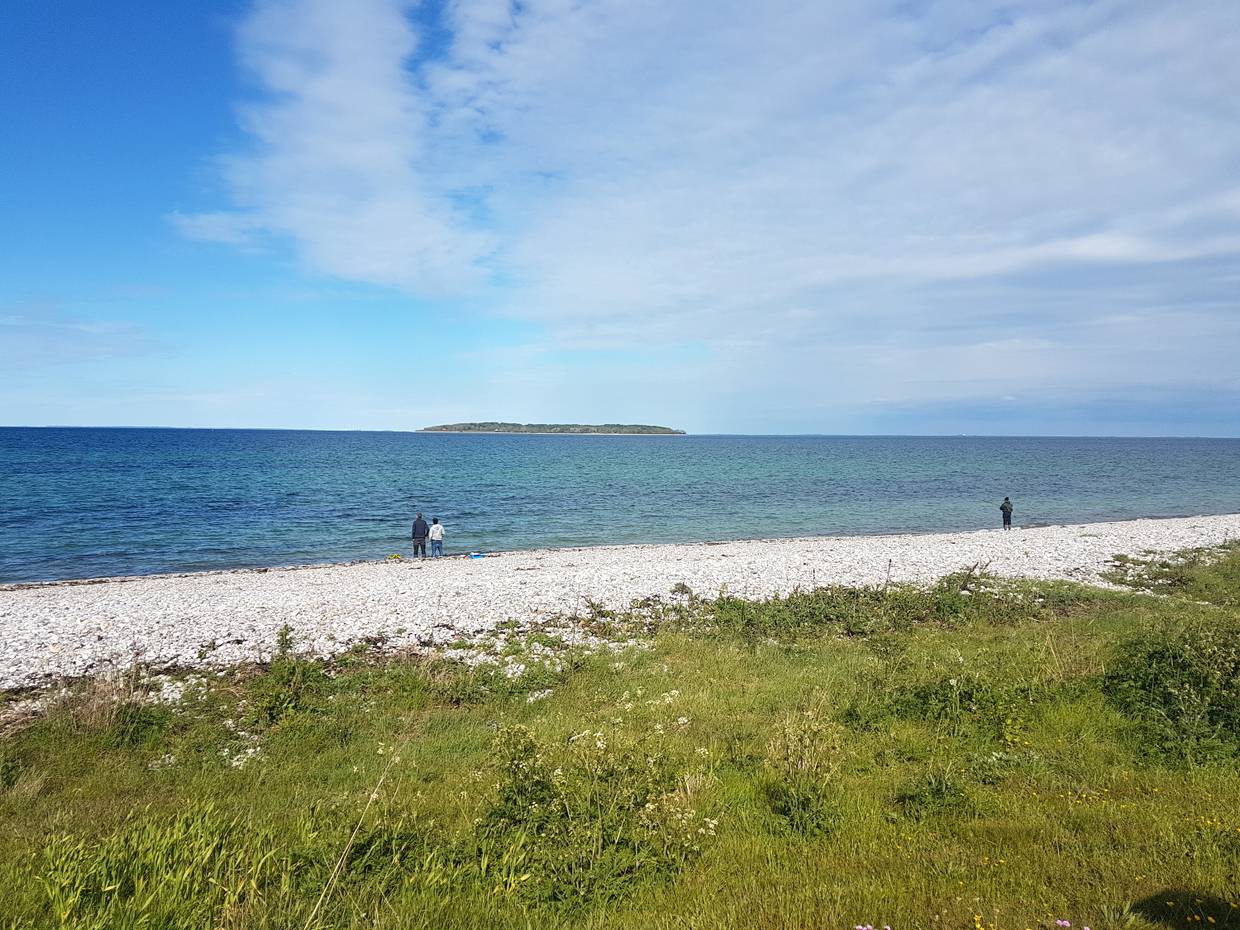 Angler am Steinstrand, im Meer eine kleine Insel