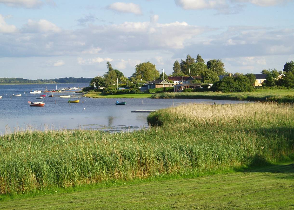 Grünes Seeufer mit Ferienhäusern, bunte Boote auf dem See