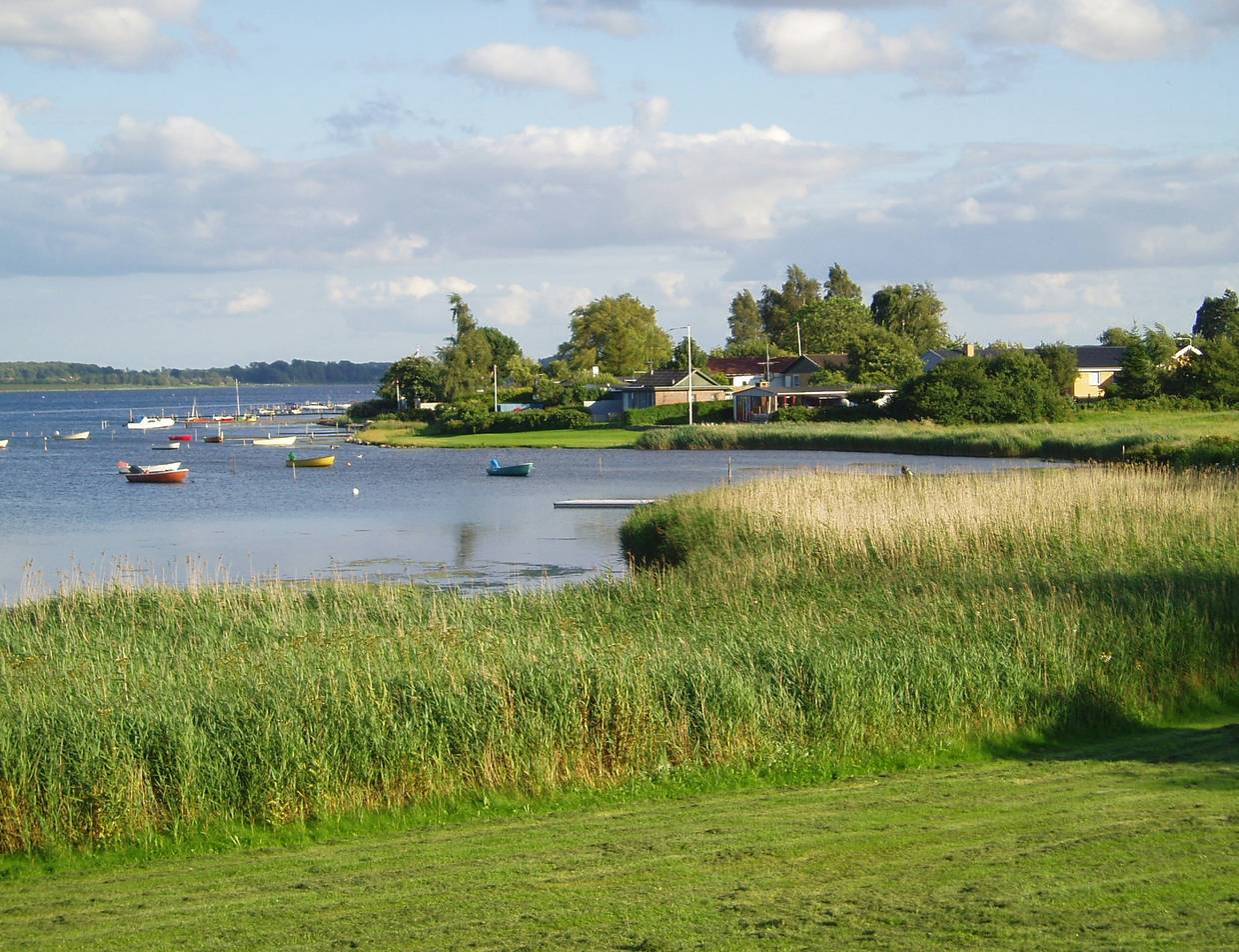 Grünes Seeufer mit Ferienhäusern, bunte Boote auf dem See