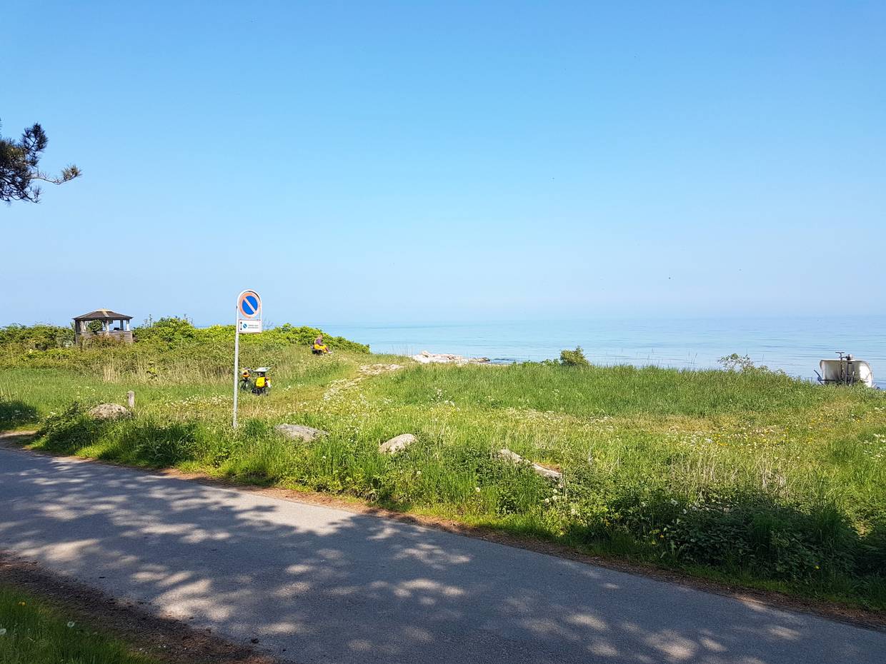 Schmale Straße, grüne Uferwiese, dahinter die flache Ostsee