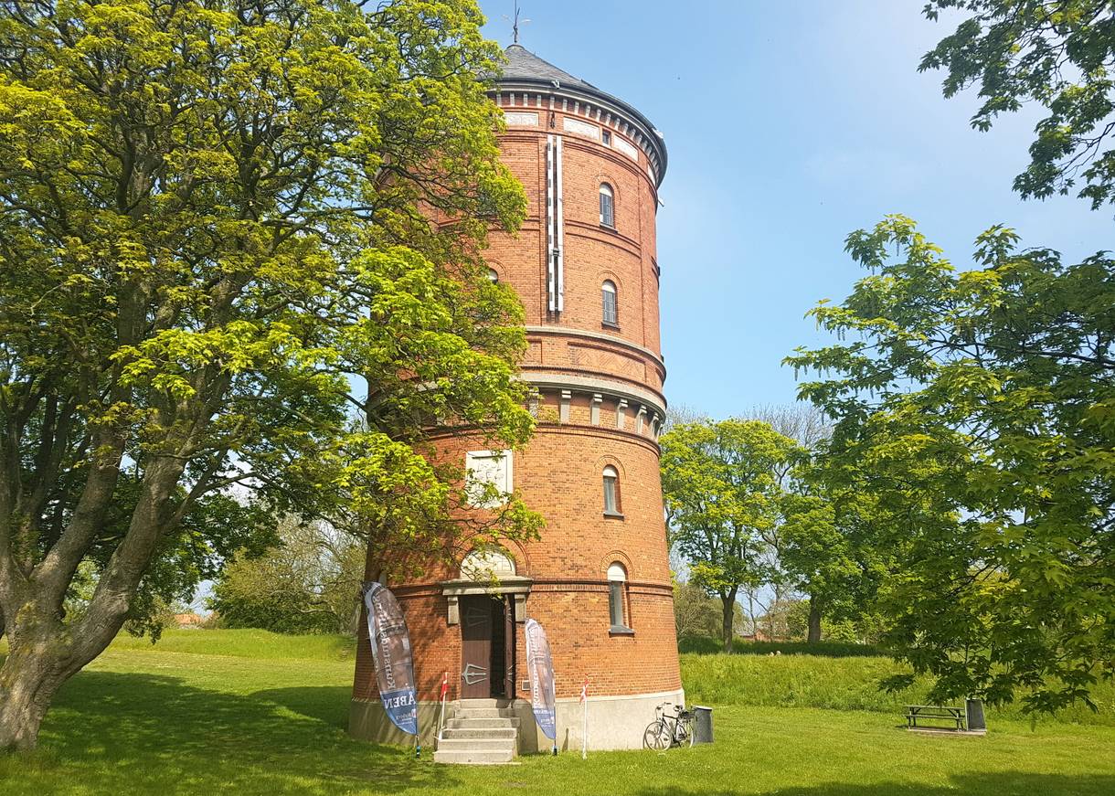 Roter Backsteinturm zwischen Laubbäumen