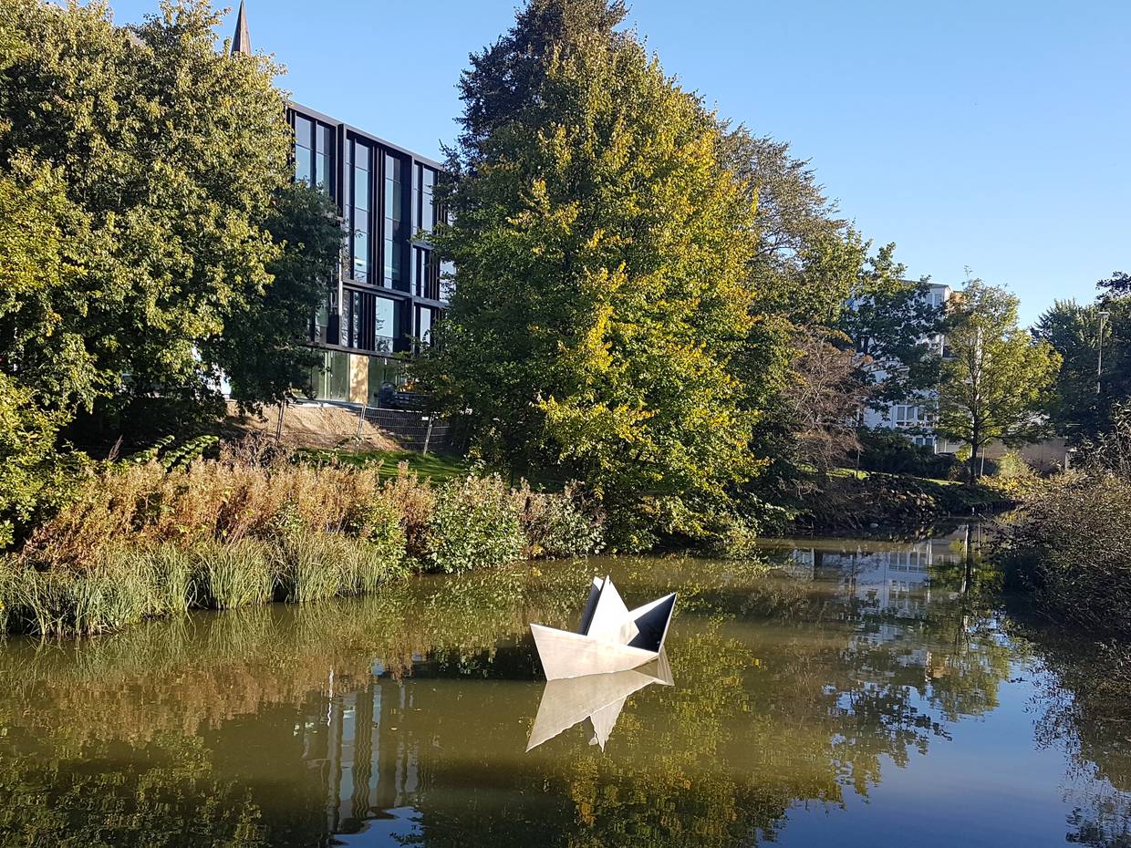 Skulptur eines Papierschiffes auf einem Bach