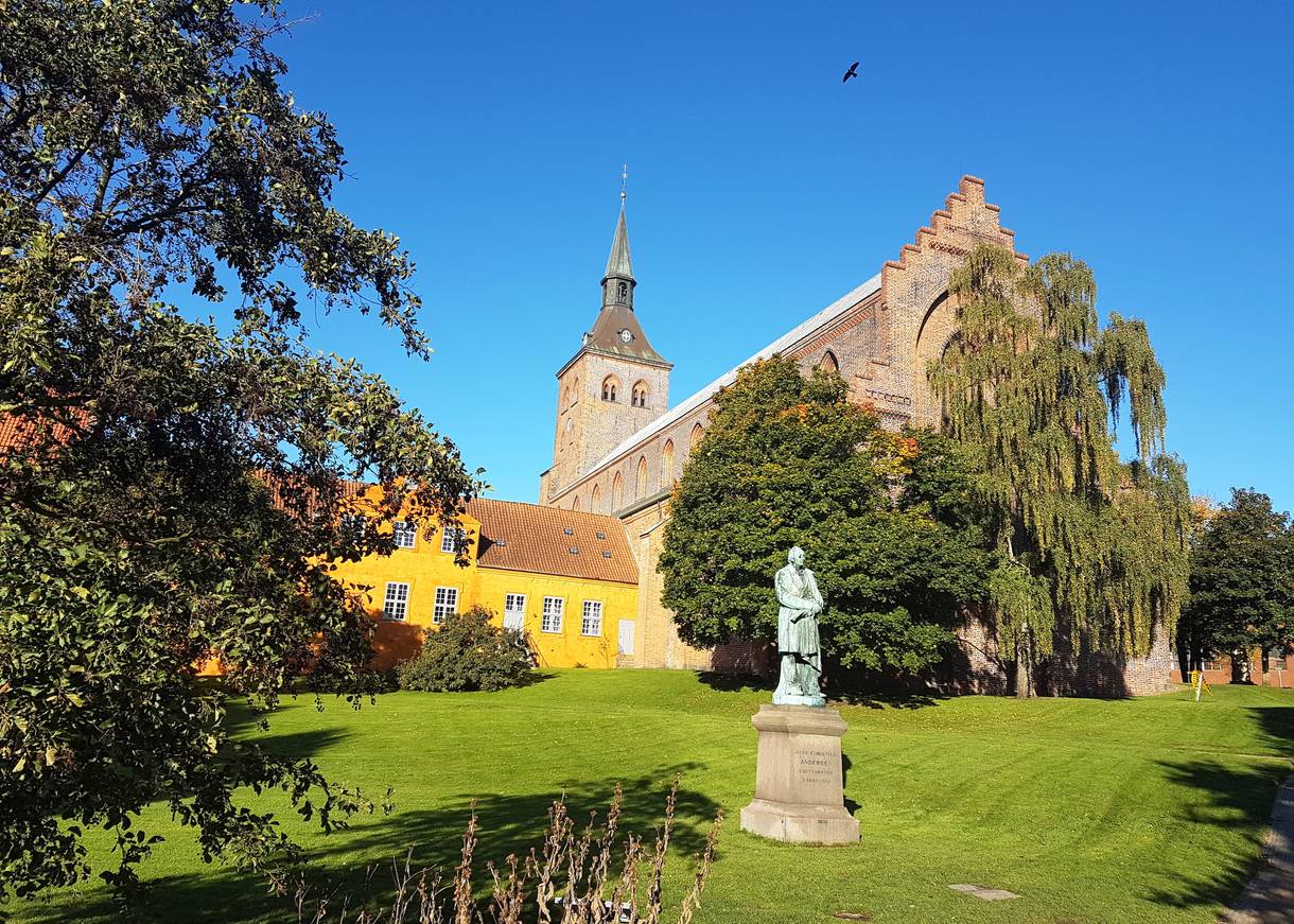 Blick auf den Odense Dom vom Park aus mit einem Denkmal für Hans Christian Andersen im Vordergrund
