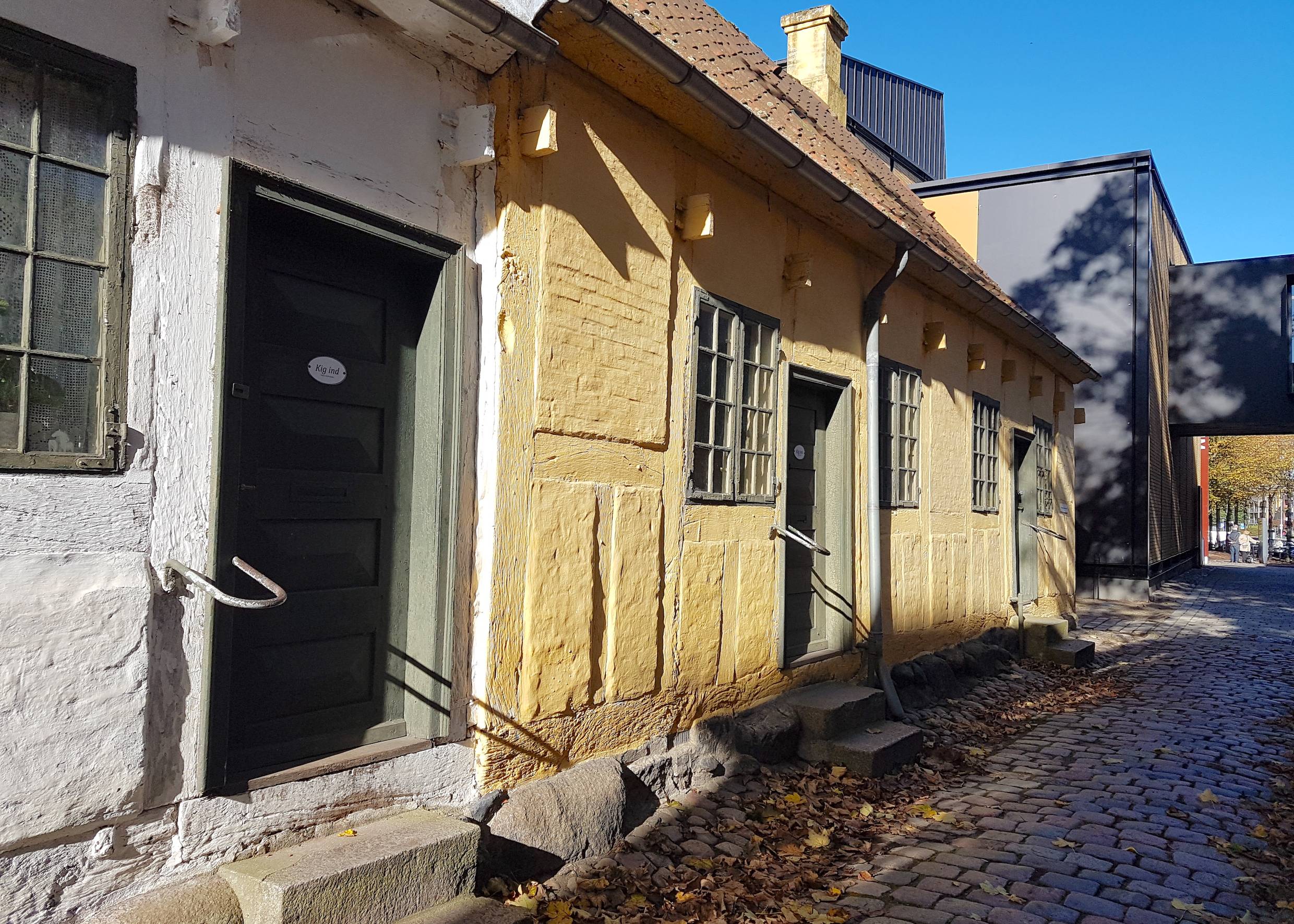 Sehr kleine Wohnhäuser, dahinter ein schwarz-roter Neubau 