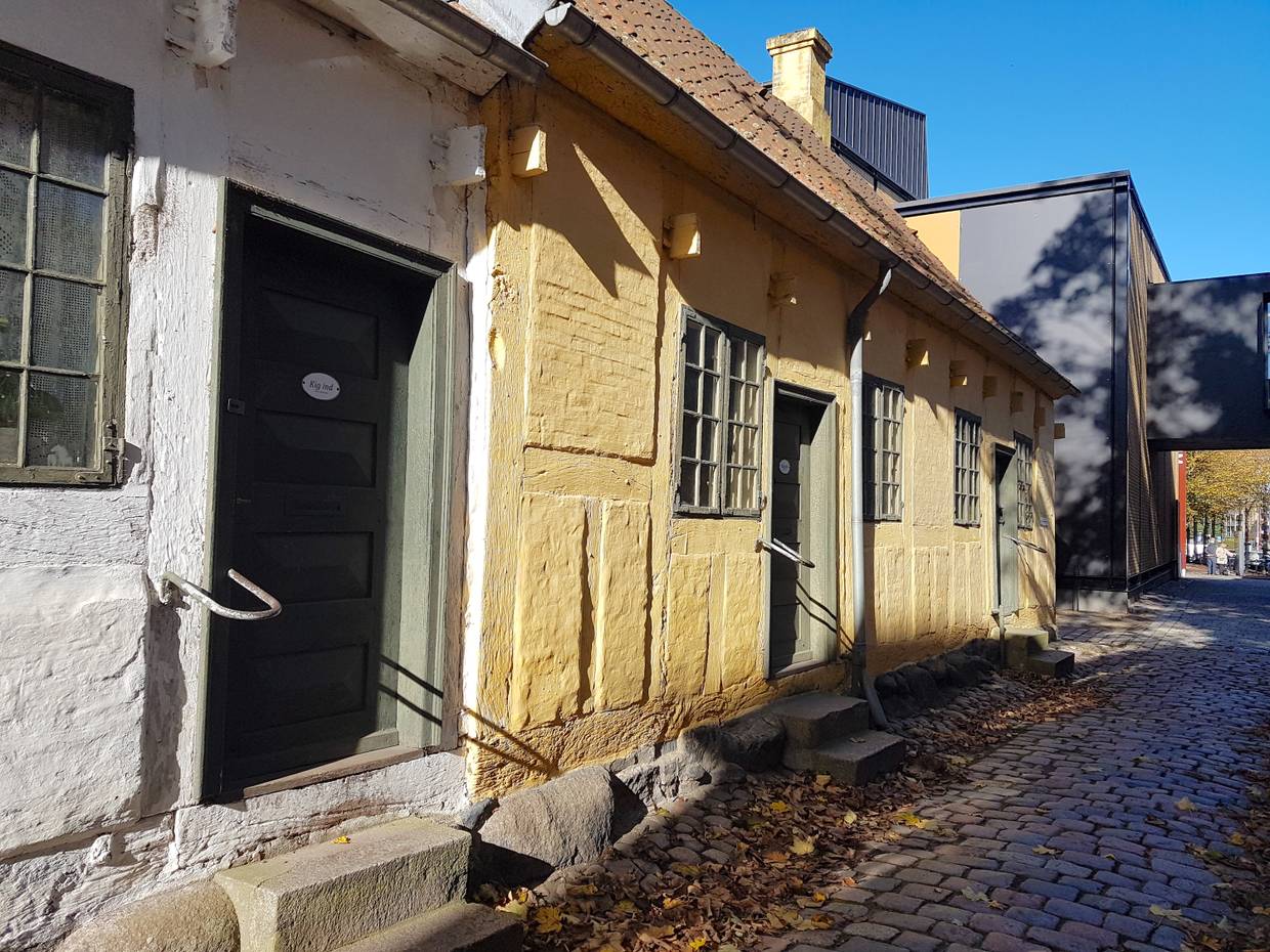 Sehr kleine Wohnhäuser, dahinter ein schwarz-roter Neubau 