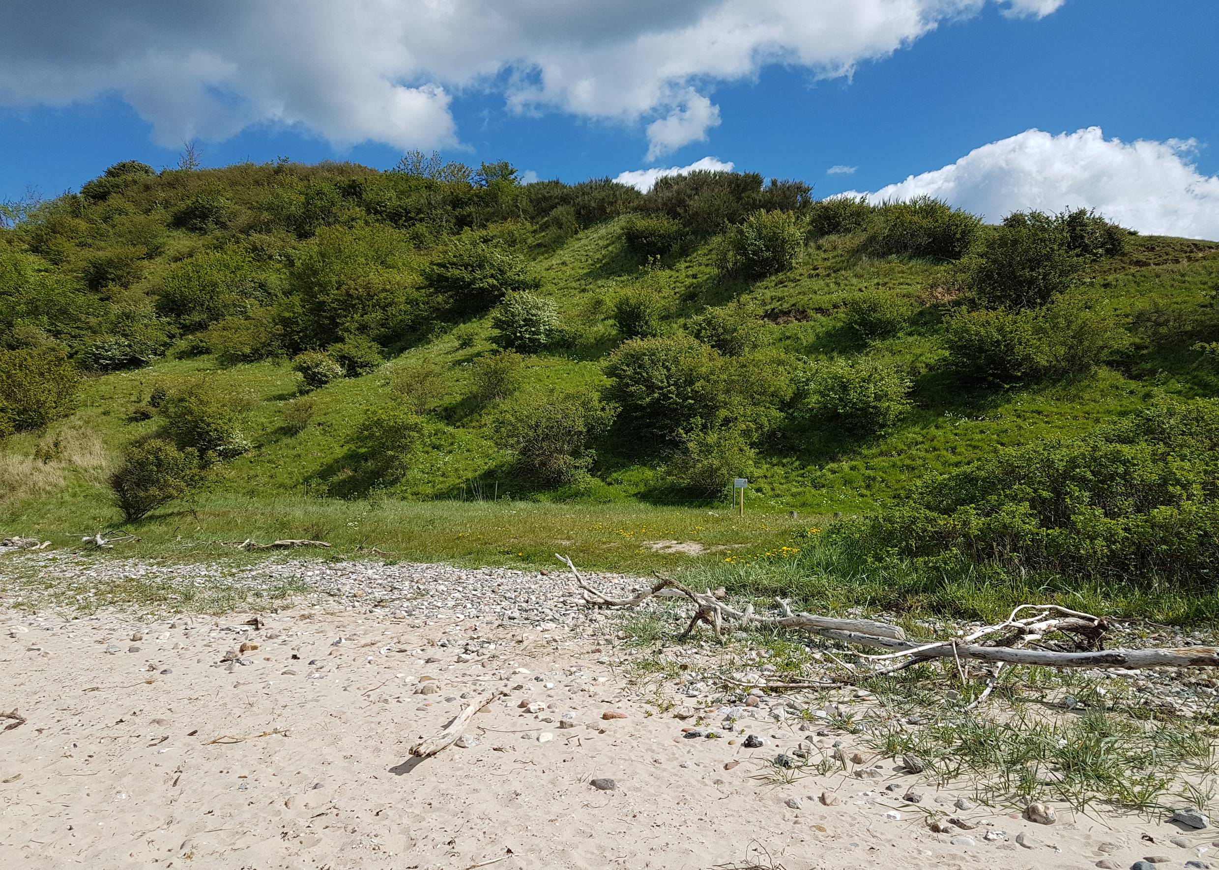 Grüner Hügel hinter einem steinigen Sandstrand