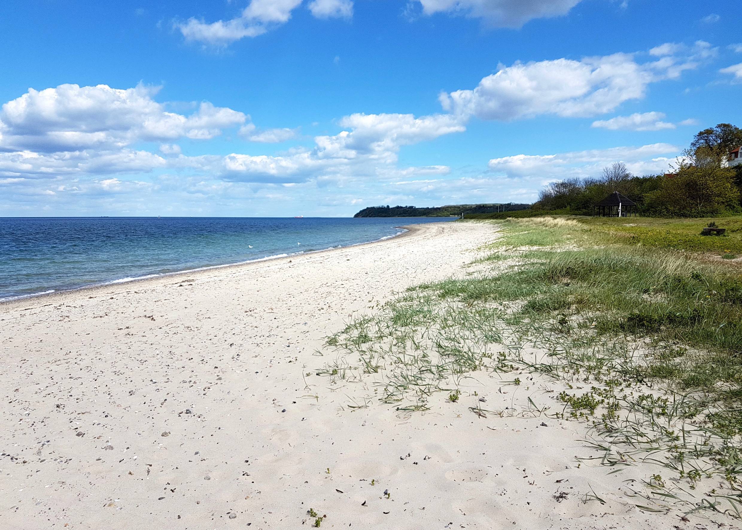 Schmaler Strand mit Häusern und einem Leuchtturm im Hintergrund