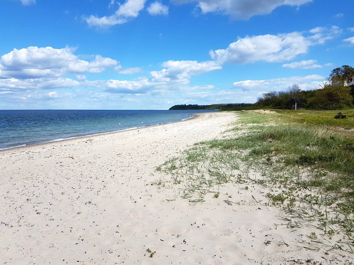 Schmaler Strand mit Häusern und einem Leuchtturm im Hintergrund