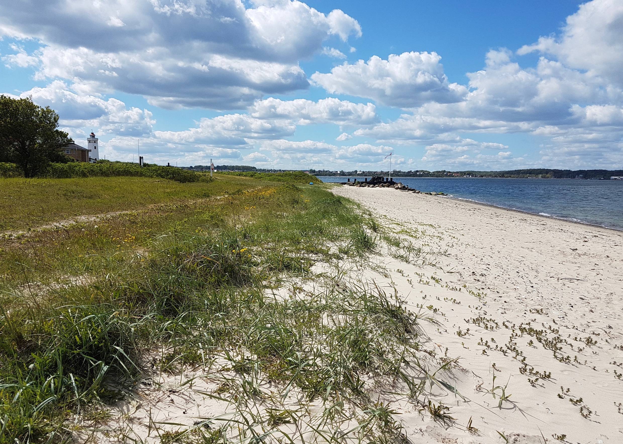 Schmaler Sandstrand mit einer Flagge und einem Leuchtturm im Hintergrund