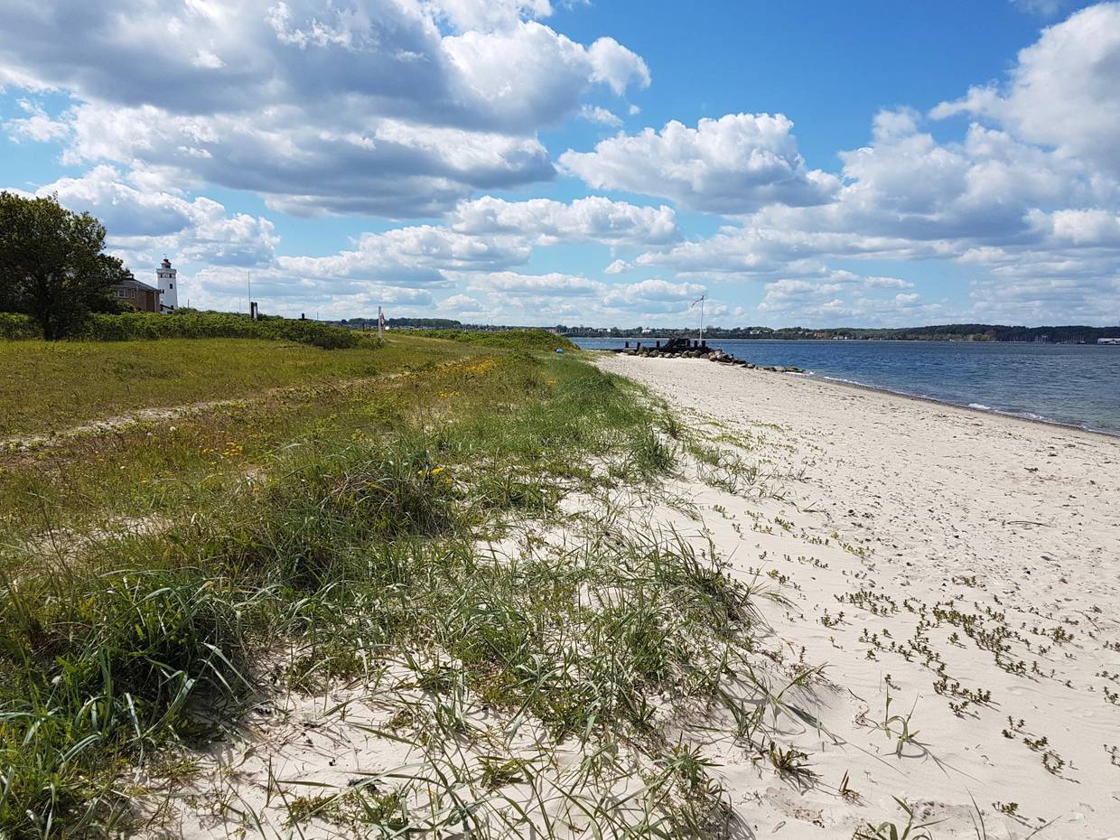 Schmaler Sandstrand mit einer Flagge und einem Leuchtturm im Hintergrund