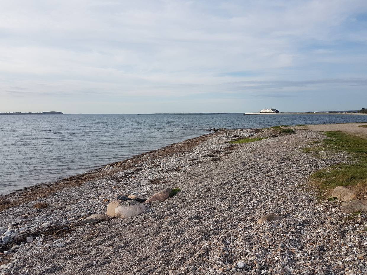 Steiniger Strand, im Hintergrund ein Fähranleger