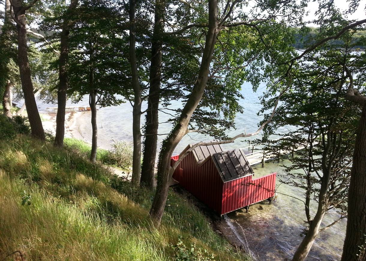 Zwei rote Badehäuser in Südfünen unter Bäumen am Fænøsund