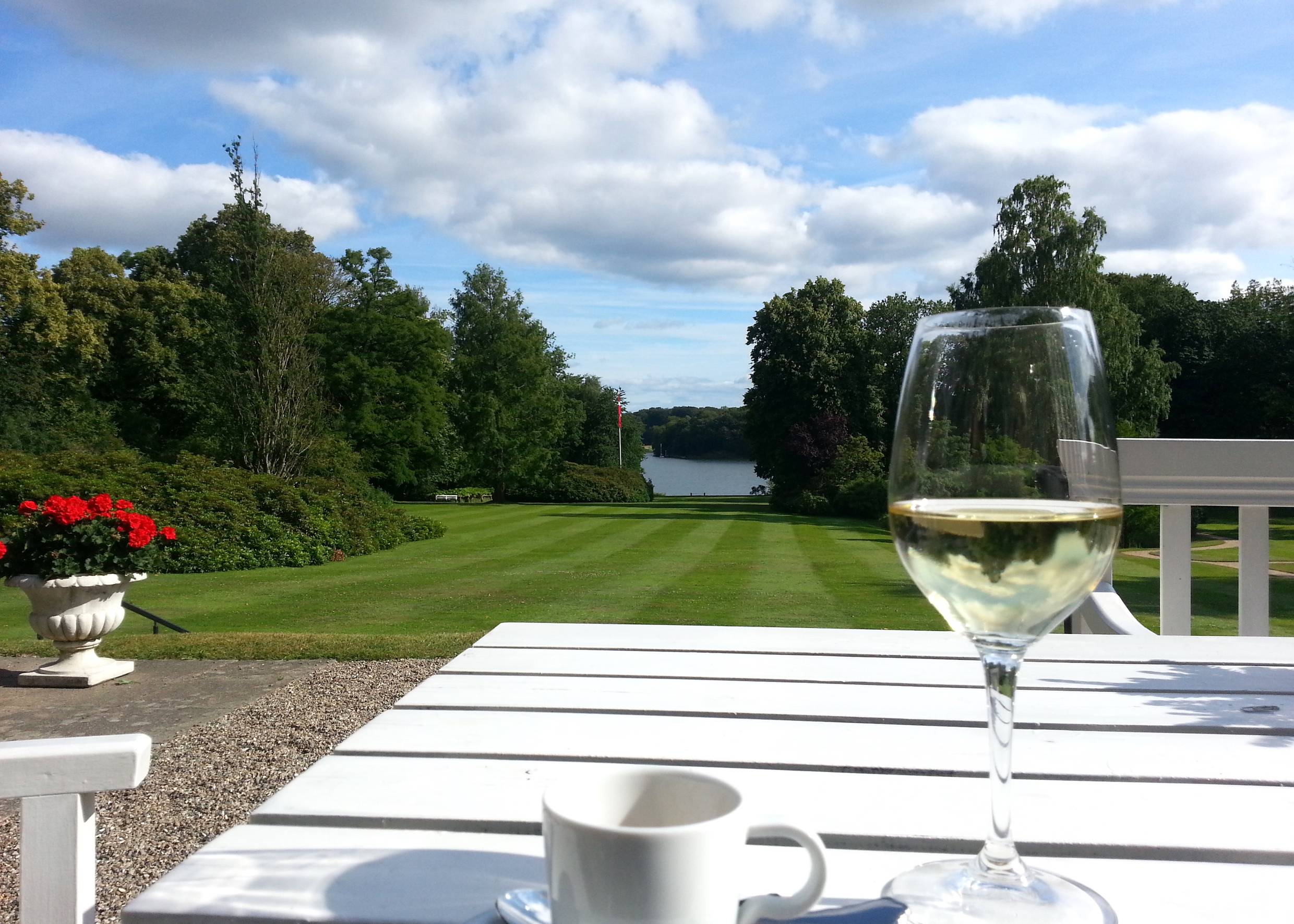Blick in einen Park über einen Tisch mit Weinglas und Kaffeetasse
