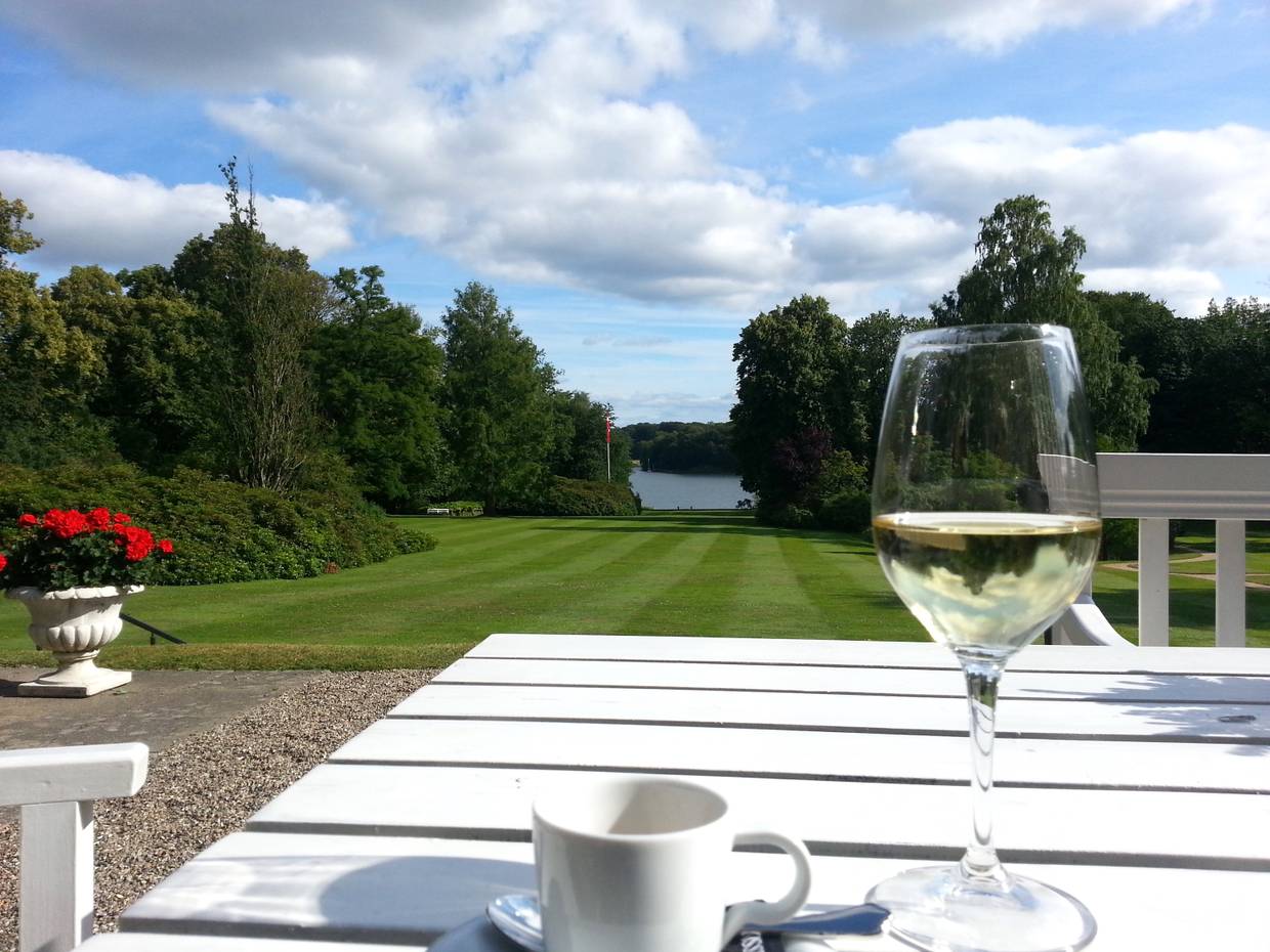 Blick in einen Park über einen Tisch mit Weinglas und Kaffeetasse