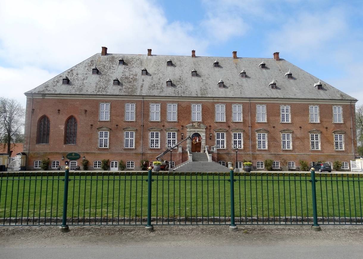 Backsteinschloss hinter einem grünen Metallzaun