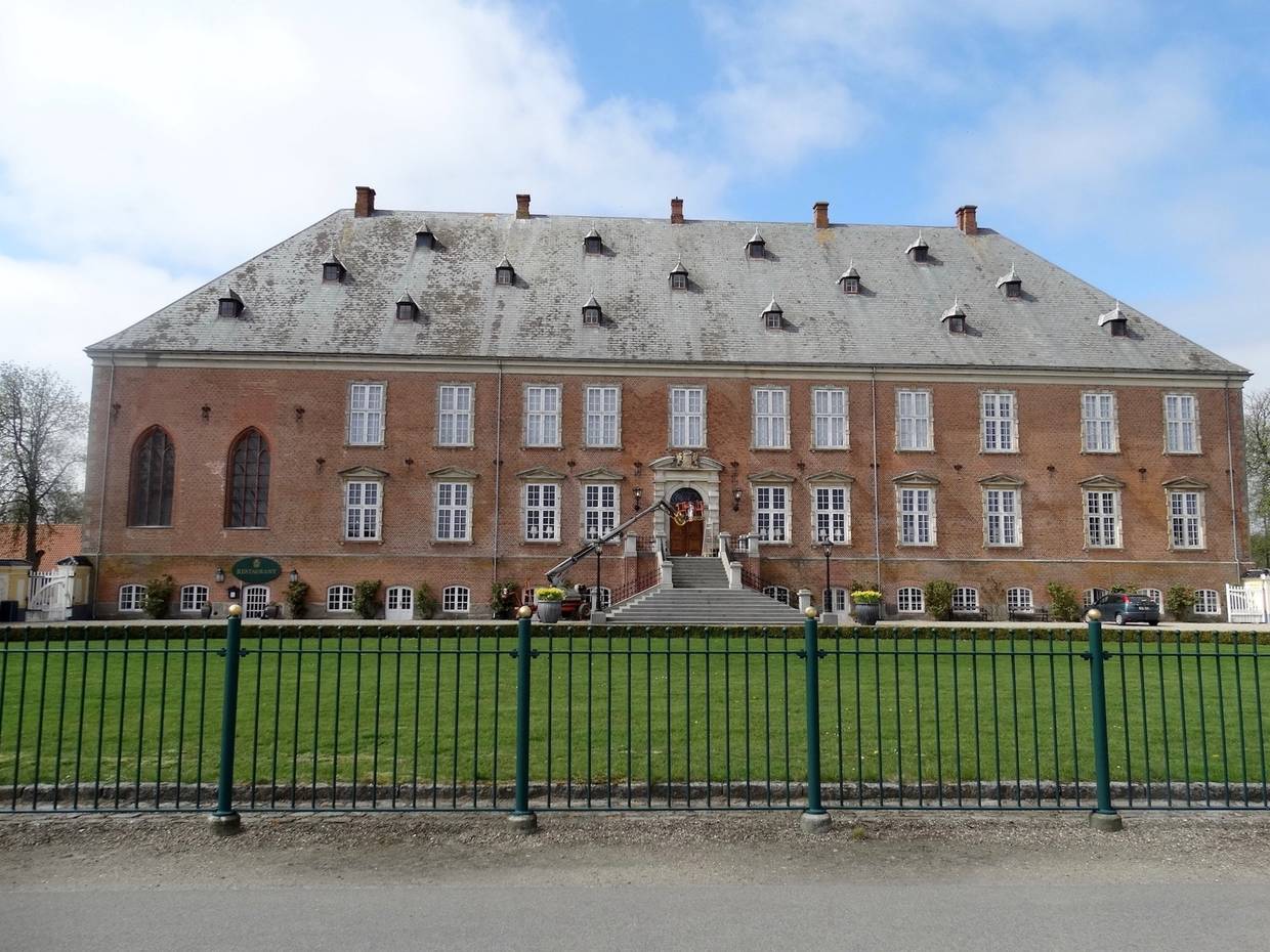 Backsteinschloss hinter einem grünen Metallzaun