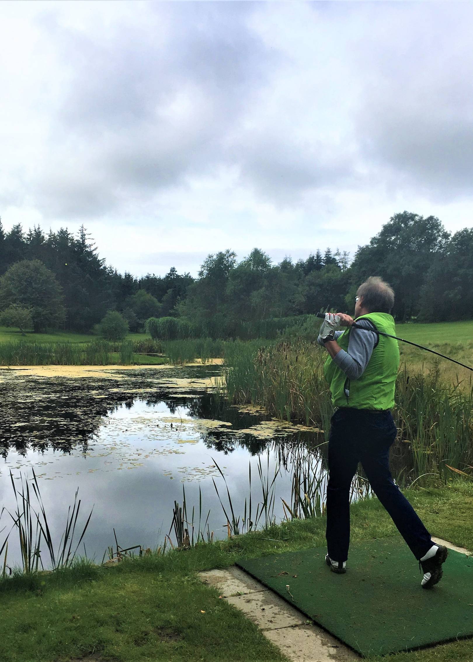 Golfspieler beim Abschlag am Ufer eines Teiches