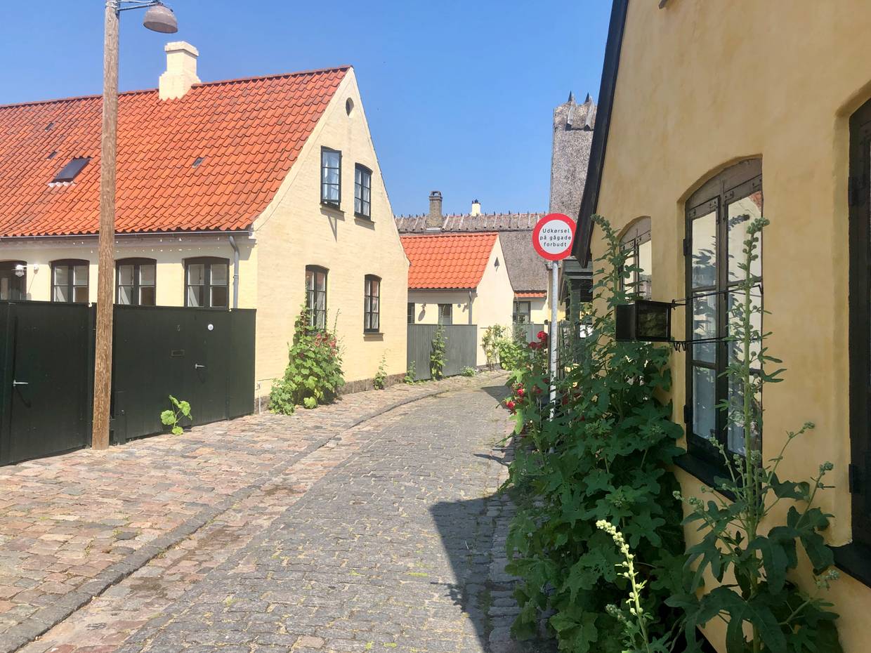 Schmale Kopfsteinpflastergasse mit gelben Häusern, davor Stockrosen