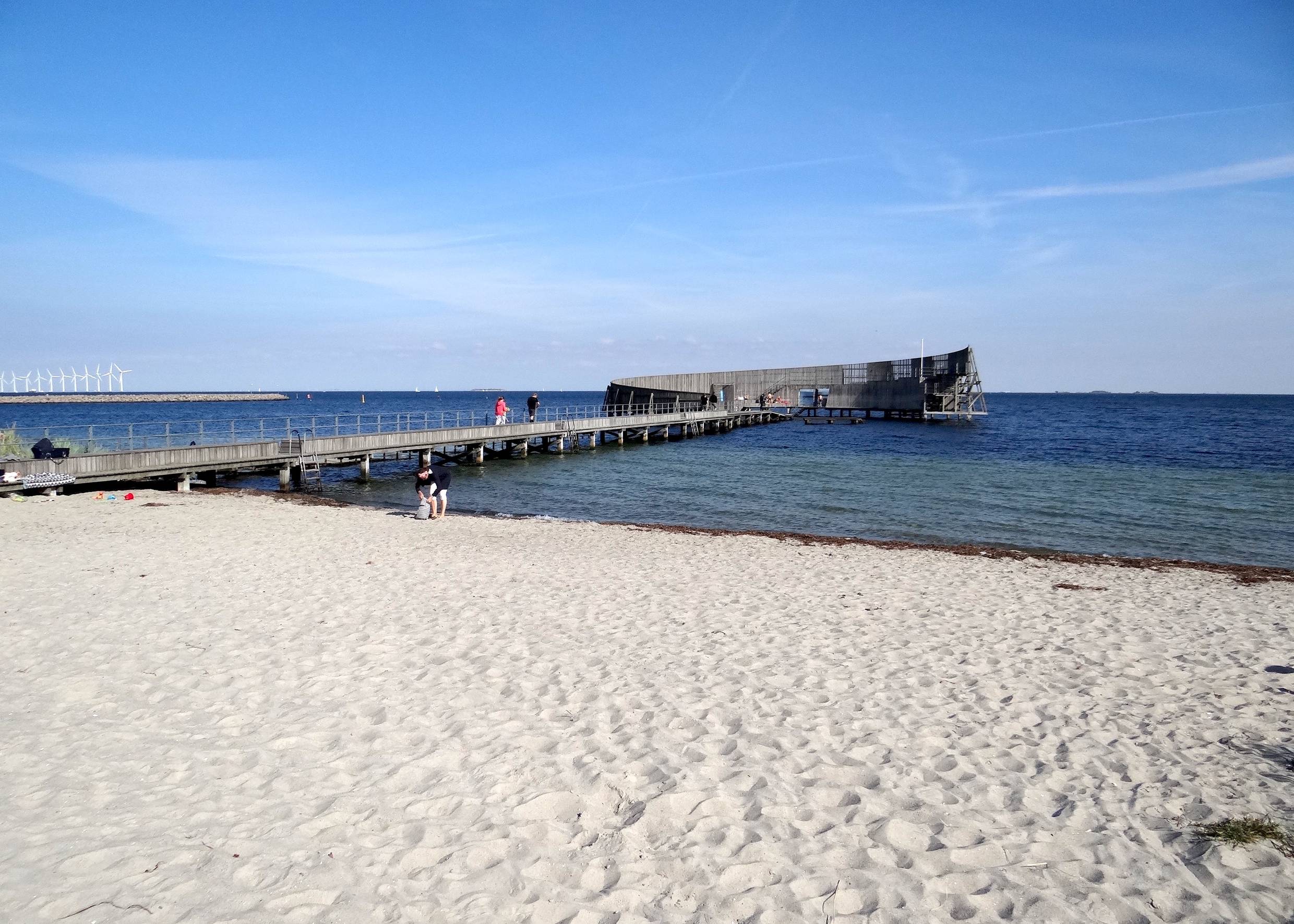 Ein runder Badesteg aus Holz vor einem weißen Sandstrand