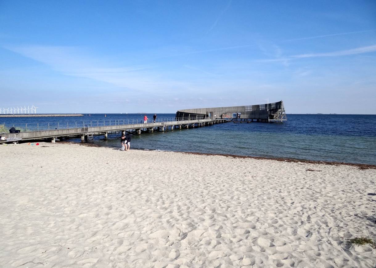 Ein runder Badesteg aus Holz vor einem weißen Sandstrand