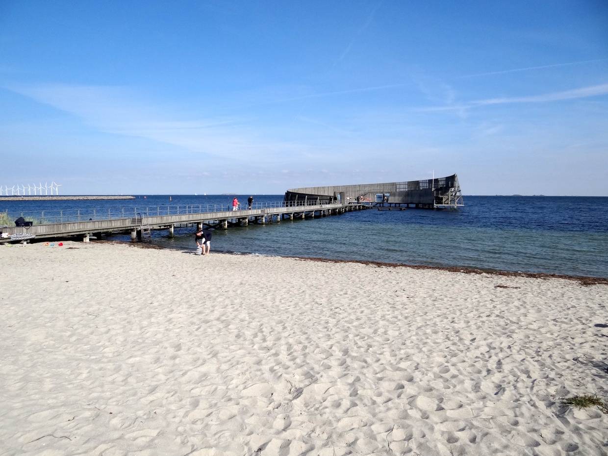 Ein runder Badesteg aus Holz vor einem weißen Sandstrand