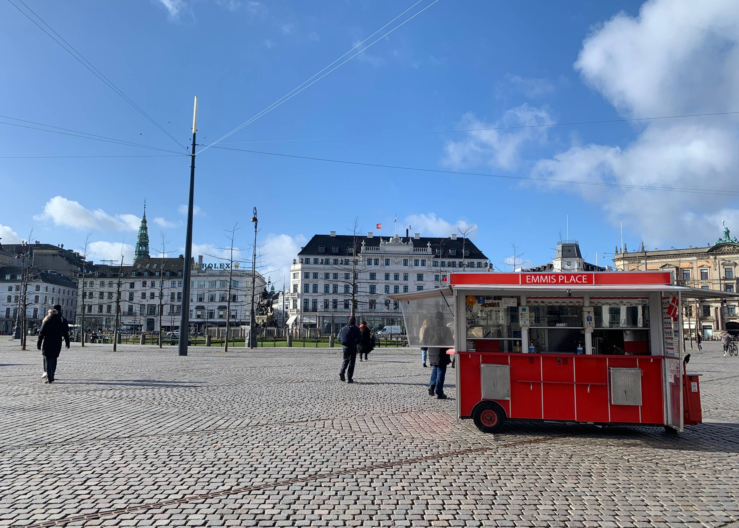 Blick über einen großen Platz, im Vordergrund ein roter Wagen, im Hintergrund ein altes Hotel