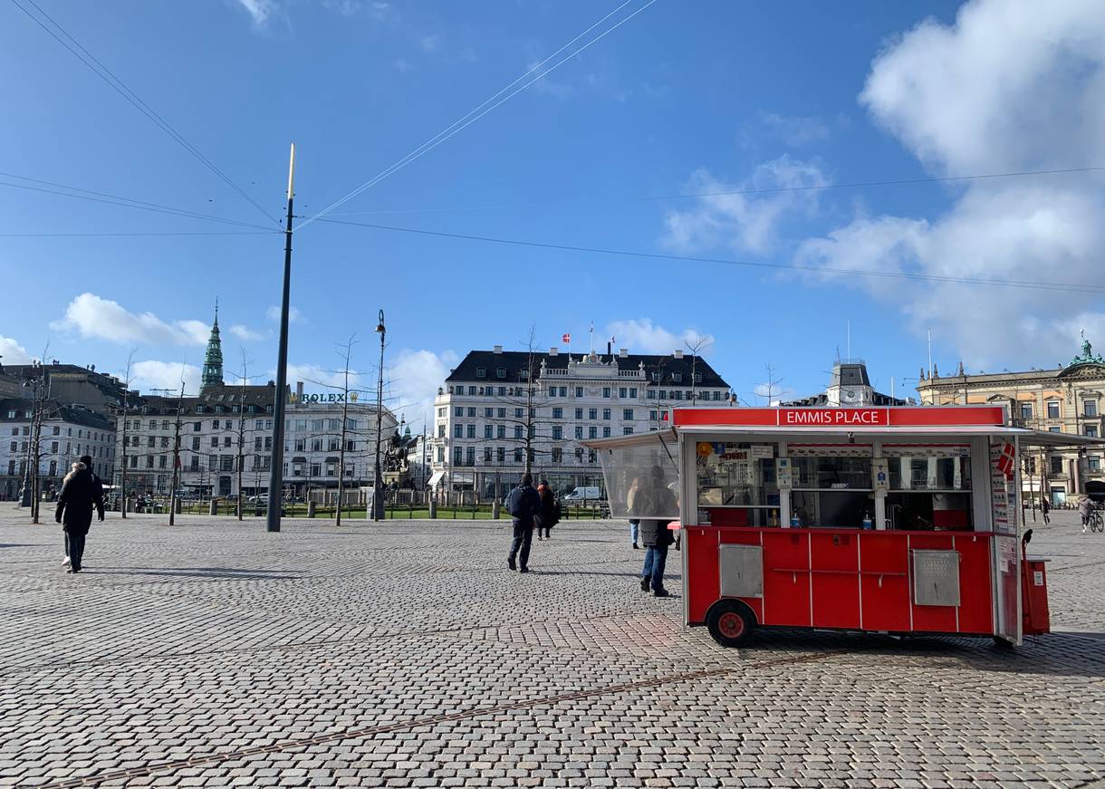 Blick über einen großen Platz, im Vordergrund ein roter Wagen, im Hintergrund ein altes Hotel