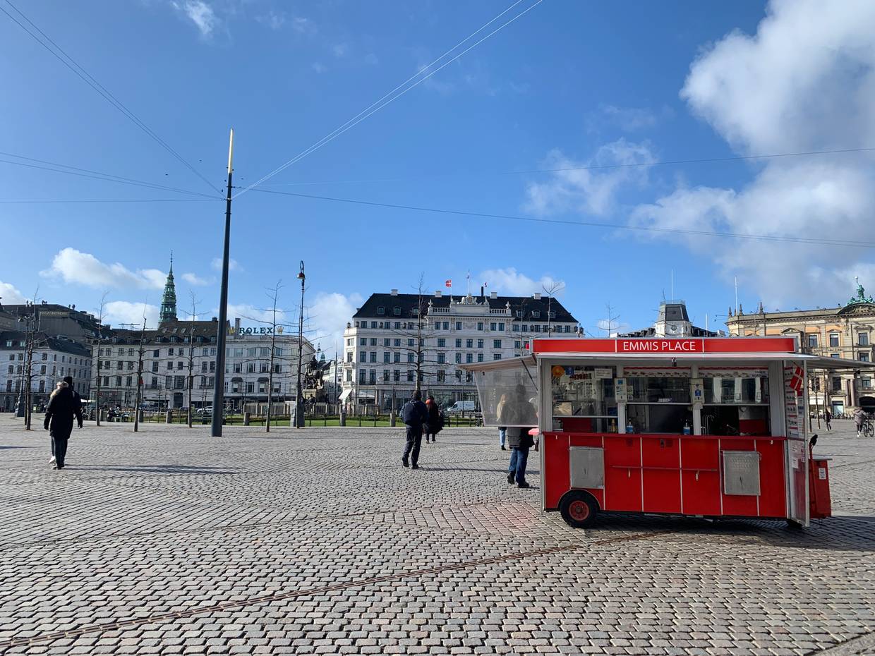 Blick über einen großen Platz, im Vordergrund ein roter Wagen, im Hintergrund ein altes Hotel