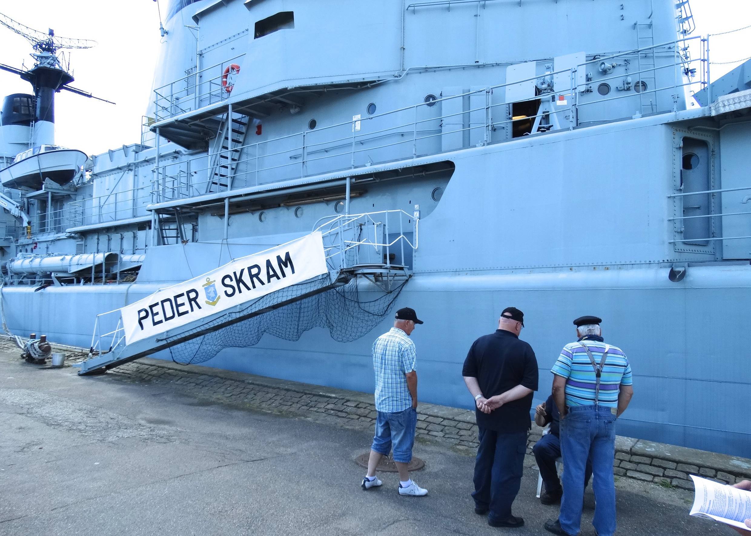 Männer vor einem ausgemusterten Kriegsschiff am Kai