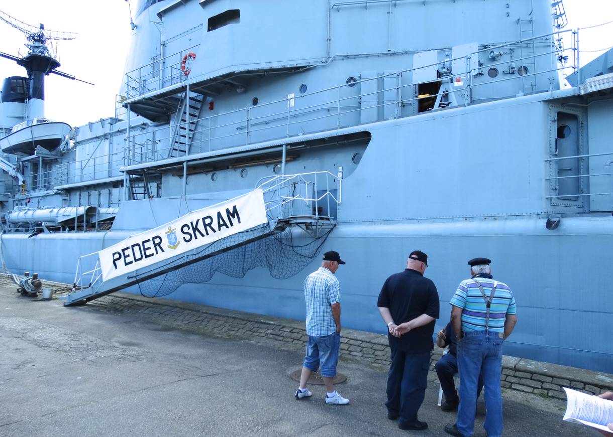 Männer vor einem ausgemusterten Kriegsschiff am Kai