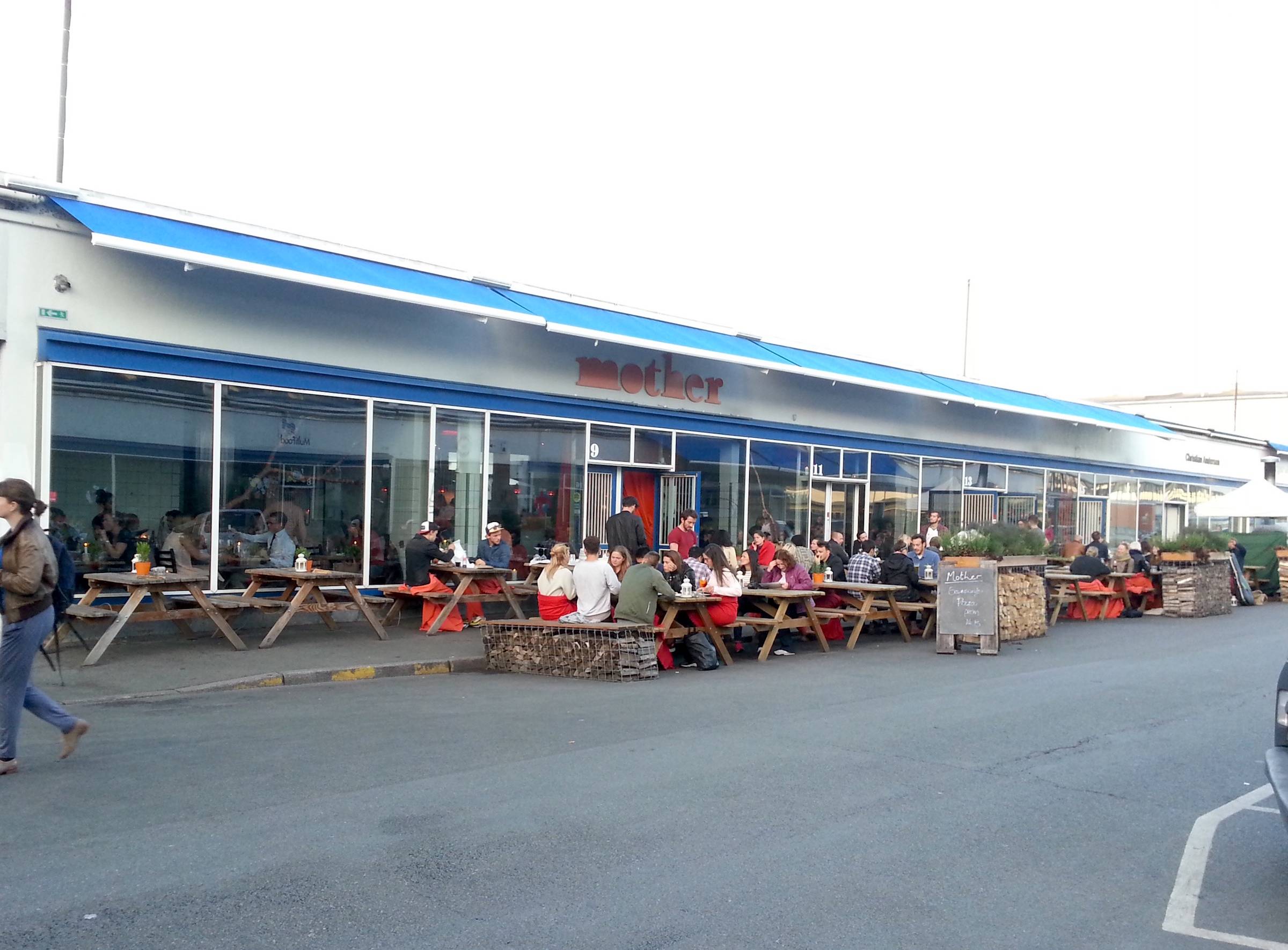 Flaches Gebäude mit blauen Markisen, davor Restaurantgäste