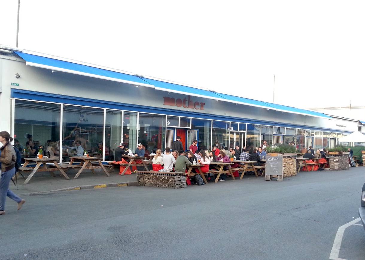 Flaches Gebäude mit blauen Markisen, davor Restaurantgäste