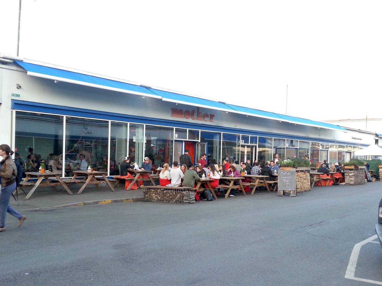Flaches Gebäude mit blauen Markisen, davor Restaurantgäste