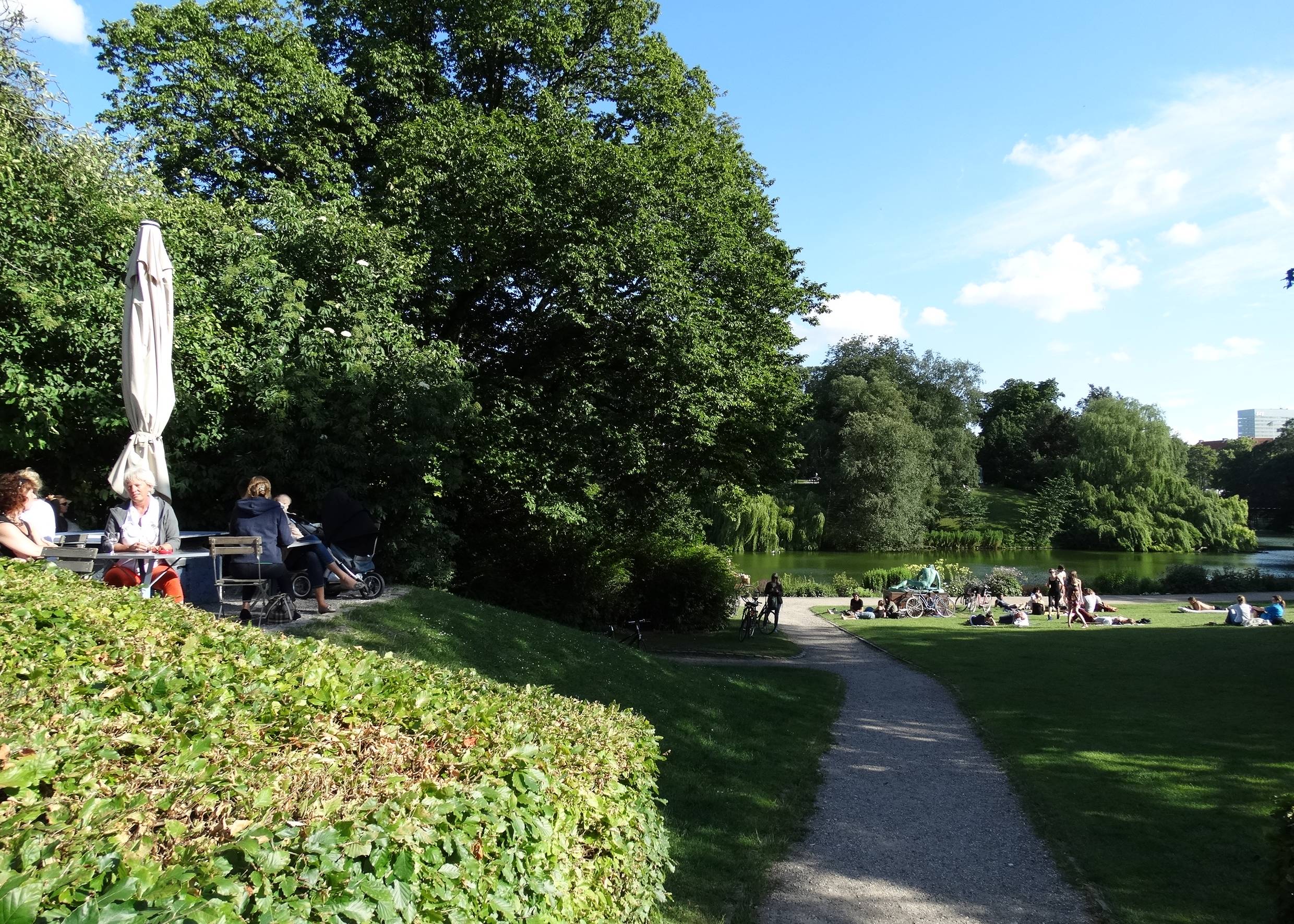 Eine Café-Terrasse und Menschngruppen auf einer Wiese im Park